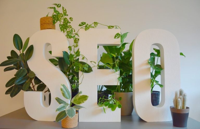 Blog Organic Seo White letters spelling "SEO" surrounded by various green plants in pots.